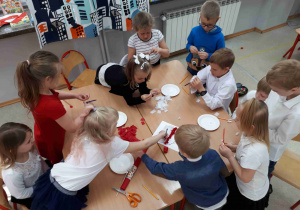 Dzieci wypełniają czerwoną i białą bibułą kontur Polski